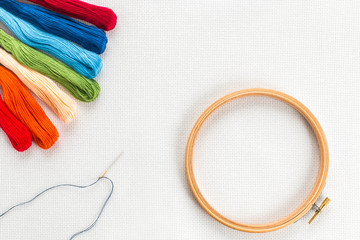 Embroidery hoop, needle and different color of thread for sewing lying on a white background. Set for needlework top view