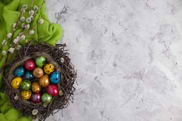 Quail eggs with willow branches for the holiday. Easter. Multicolored eggs in a nest on a light background. The view from the top. Copy space