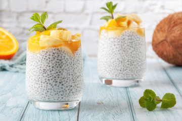 Chia pudding with banana in two glass glasses with raw chia seeds on a blue wooden table