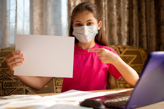 Young schoolgirl in medical mask pointing to blank cheet of paper for inscription. Concept of distance learning