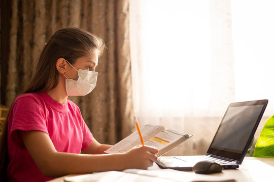 Hard-working school learner girl in medical mask, holding book, having online lesson at home, communicating with teachers, classmates, doing tasks at the computer