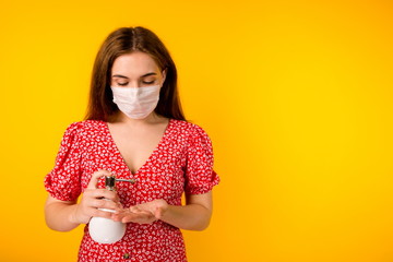 Girl in a medical protective mask on her face, taking care of herself, holds a bottle of antiseptic in her hand, treating her hands from viruses, on a yellow background