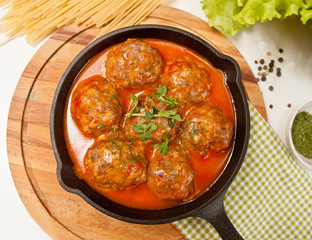 Meat balls in spicy tomato sauce with herbs in a iron pan.