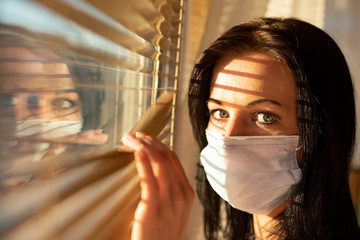 Woman with surgical mask looking out of home window, concept of quarantine during viral pandemic...