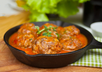 Meat balls in spicy tomato sauce with herbs in a iron pan.