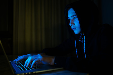Hacker is  hacking into the computer network. Young boy in a dark room with laptop.  Hacker with a laptop.