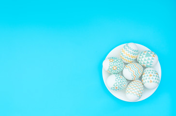 Decorated Easter eggs lie on the white plate on blue background. Happy Easter holiday concept. Greeting, invitation card. Flat lay style with copy space.