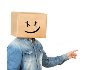 Hombre con caja de cartón en la cabeza con cara sonriente y con la mano levantada señalando hacia arriba y a un lateral sobre un fondo blanco. Vista de frente. Copy space - obrazy, fototapety, plakaty