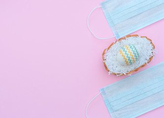 Fototapeta na wymiar Decorated Easter egg in the basket and medical face masks on the pink background. Happy Easter during coronavirus, quarantine, stay home, social distance, COVID-19 concepts. Flat lay with copy space