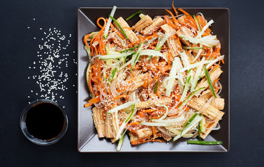 Fuju salad with bean noodles, pickled carrots, cucumbers and sesame seeds on a dark background. Next to soy sauce. Asian cuisine