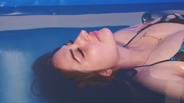 Beautiful girl in bikini relax enjoy closes eyes in blue water Spa pool bath.