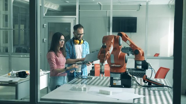 Robotic arm in motion is being observed by two engineers