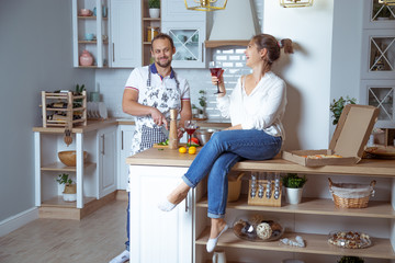 man and girl in the kitchen, eat pizza, drink wine and laugh merrily