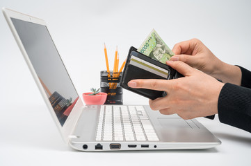 E-commerce concept. A man's hand pulls money out of his wallet in front of a laptop monitor.