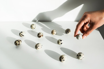 Woman hand take one quail egg from heap of other on white background. Right choice. Unusual easter concept.