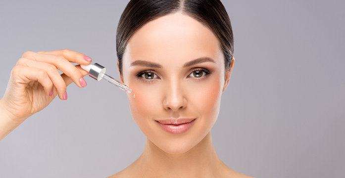 Skin care concept. Beauty portrait of smiling young woman girl holding pipette with cosmetic oil  or  serum near clean face. Cosmetology and Spa