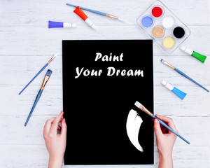 Mock up / mockup for drawing.  Hands holding empty black board and brush with sigh "Paint your dream".  View from above