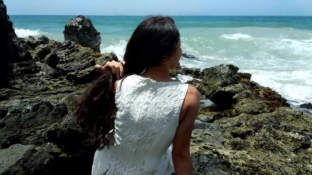 Latina girl sitting on a rocky shore near the sea
