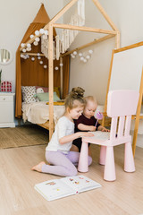 The sisters play together in their large, sunny and bright room. They do not leave the house in self-isolation mode in an epidemic. Girls do their homework. Kids play and smile. Supporting each other 