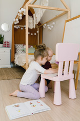 The sisters play together in their large, sunny and bright room. They do not leave the house in self-isolation mode in an epidemic. Girls do their homework. Kids play and smile. Supporting each other 