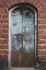 Arched shades of blue and brown wooden door sits in the middle of a red exposed brick wall. 