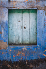 Vintage wooden window in teal surround by a wall with chipped paint in a shades of blue.