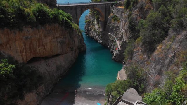 Aerial view inside bay of Fiordo di furore beach. Incredible beauty panorama of a mountains paradise. The rocky seashore of southern Italy. Sunny day. Stone bridge traffic, cars and motorcycle. Amalfi