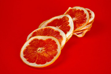 Chips of dried grapefruit sliced in thin circles, shot on a red background. Background for vegetarianism, healthy and wholesome food.