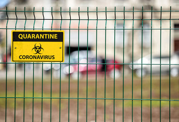 Coronavirus Quarantine sign on green decorative metal wire fence, the city street silhouettes are visible behind the fence