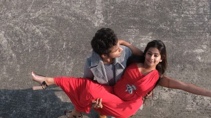 An young Indian Bengali brunette man in western wear taking his girlfriend moving in a slow circular motion on the rooftop. Indian lifestyle and holidays.