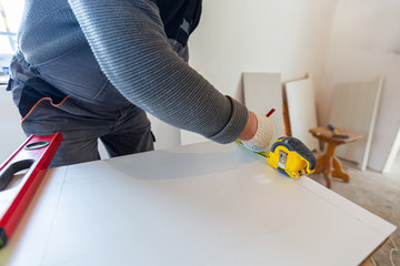 Worker is measuring the plastic detail before it cutting in apartment that is under construction,...