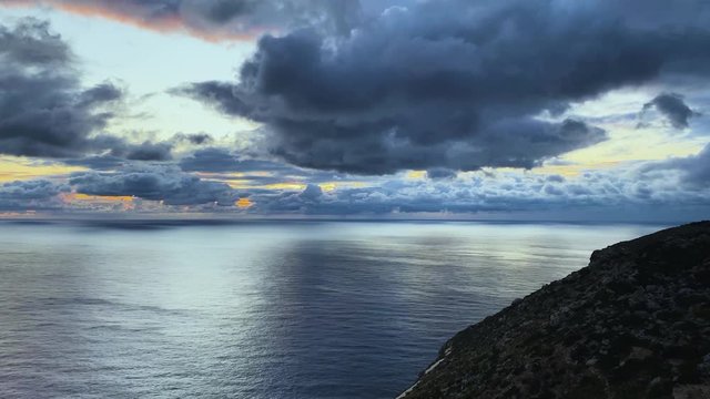 Fluffy dark large clouds drifting over the calm sea right after the sunset.