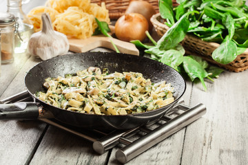 Tagliatelle pasta with spinach and mushrooms on a pan.