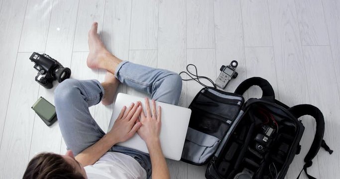 Top View of a Young Hipster Photographer Finished Working on Laptop With Green Screen. Backpack, Medium format film and DSLR Camera, External Hard Drives and Light Meter. Freelancer Closing Notebook