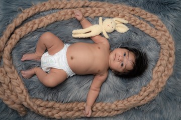 Adorable baby in diaper lying on a grey blanket having teddy bear