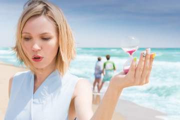 End of vacation. A woman holds an hourglass against the background of the sea, the ocean.