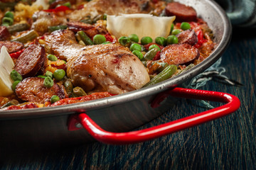 Traditional paella with chicken legs, sausage chorizo and vegetables served in paellera