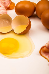 Broken chicken egg, chicken eggs, slices of bacon and sausage and tomatoes on a white background. Close up.