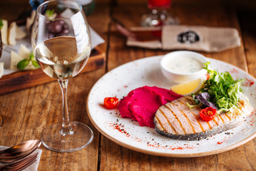 appetizing grilled salmon on a white plae with sauce and glass of wine, horizontal, side view