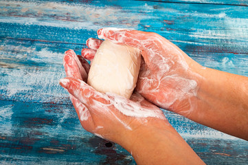 Someone is soaping their hands with a piece of toilet soap on a wooden background. Close up. Hand...