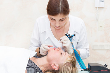 Lip tattoo and correction of the shape of a middle-aged woman in a beauty salon.
