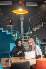 Beautiful two girls with hijab hanging out, typing on laptop, learining about photography and study