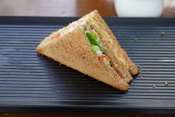 A single Tuna sandwich on black serving plate. One Club Sandwich with chicken, ham, cheese, tomatoes, cucumber, bacon, lettuce, herbs and toasted bread. Front view with blurred background.