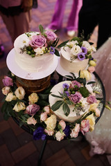 Cream wedding cake with flowers stands on a glass table.