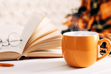 Autumn cozy composition. Book, plaid, steaming cup coffee or hot drink. Autumn or winter concept of coziness and interior. Front view, copy space