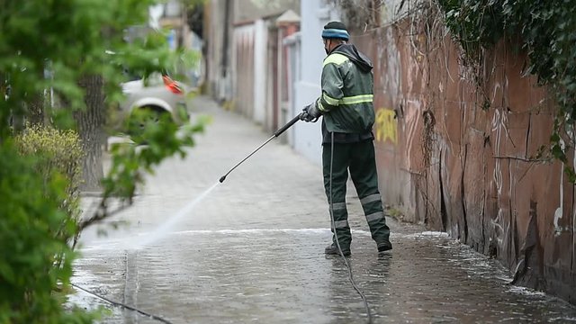 Public janitor deep cleaning the sidewalk with high pressure disinfectant solution in times of corona virus pandemic in a lockdown Bucharest, Romania.