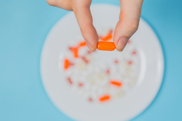 Hand holding orange pill. different pills on white plate on blue background. health and medicine