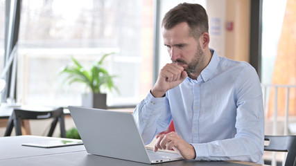 Sick Young Man with Laptop Coughing in Office