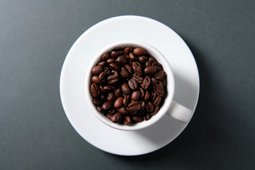 White cup of coffee with grains on a dark background, top view