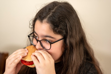 Young girl eats hamburger. Close up.